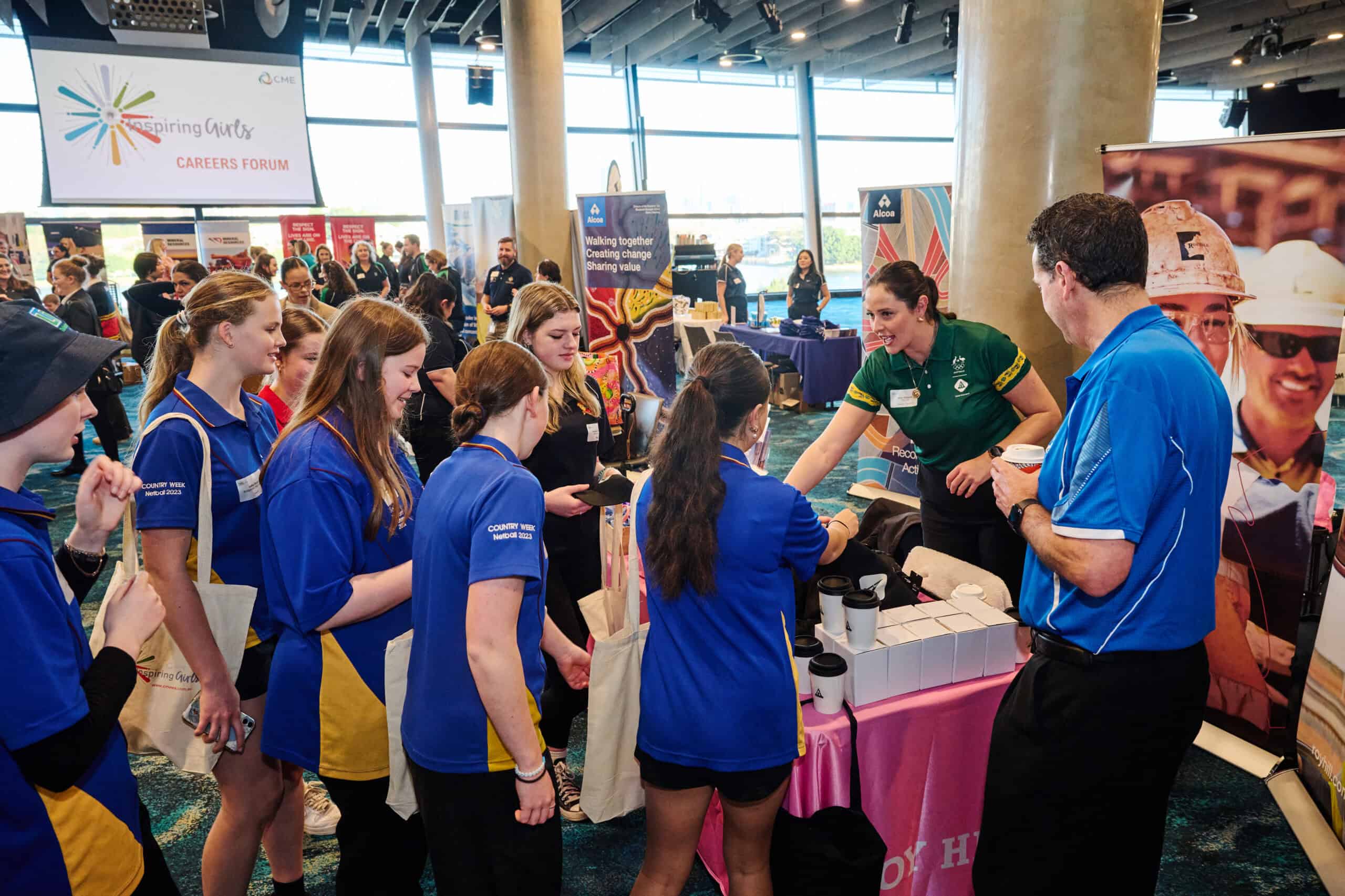 Blue-shirted students attending the CMEWA career expo and engaging with industry representatives at an indoor event.